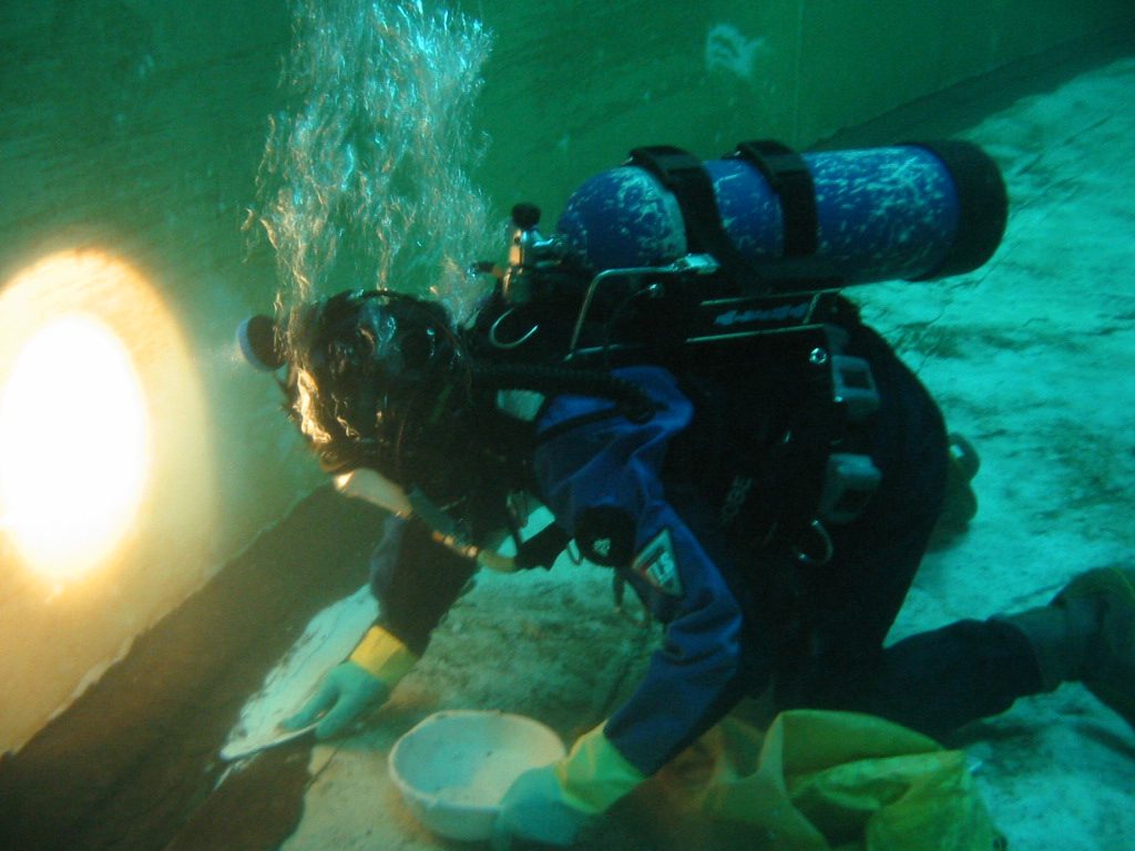A diver uses a plastic mixing bowl and spatula to apply underwater epoxy in a crack repair situation.