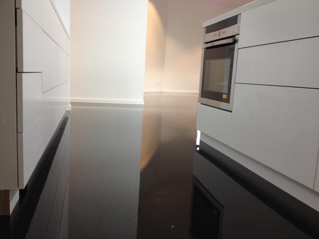 A low-angle shot of a high-gloss, black decorative floor installed in a sleek residential kitchen.