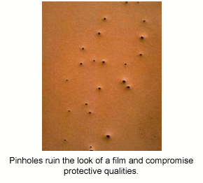 A close-up photo of large, visible pinholes in a brown protective epoxy coating.