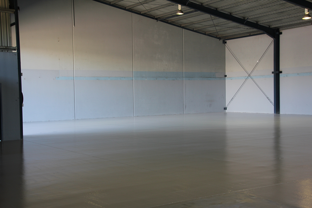 A large, empty warehouse of a manufacturing company with a new commercial floor installed.