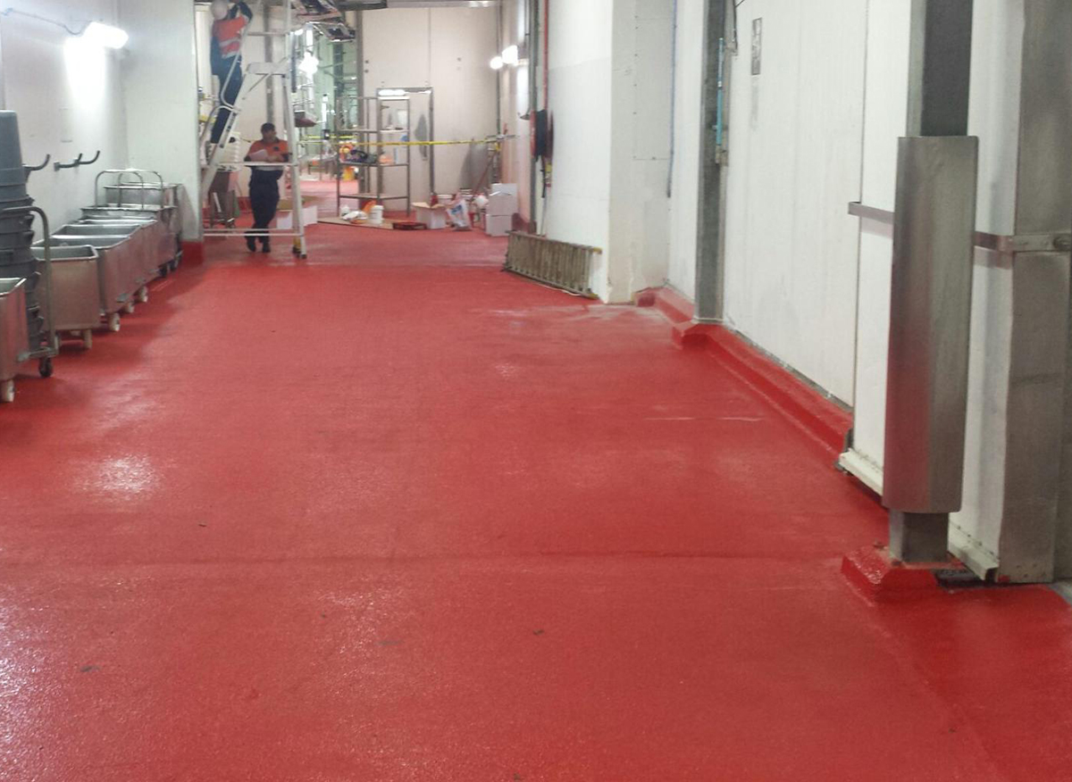 A red non-slip commercial floor extending down the walkways of a large abattoir.