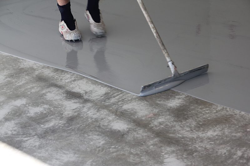 A specialist epoxy floor coating being applied with a squeegee onto concrete.