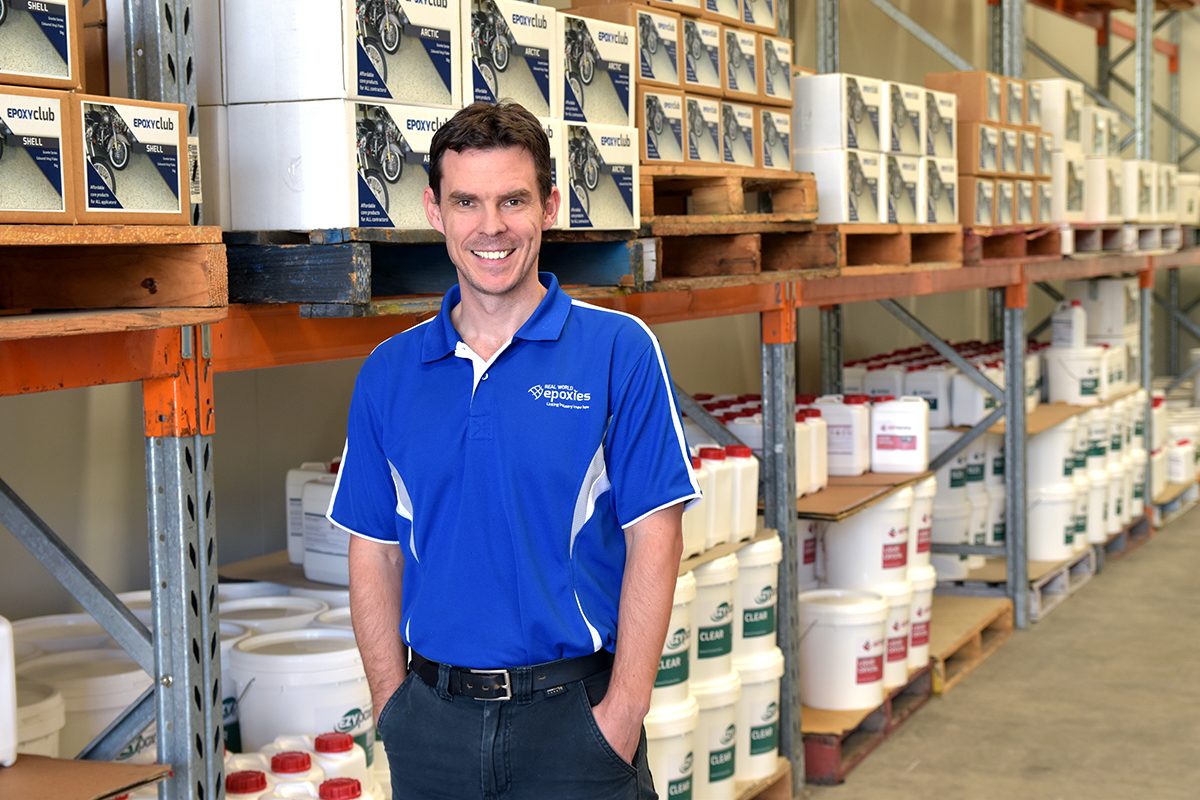 An epoxy flooring manufacturer standing in front of the products stored in their warehouse.