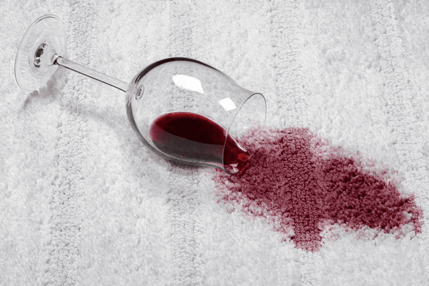 A tipped wine glass on carpet creating a large red stain.
