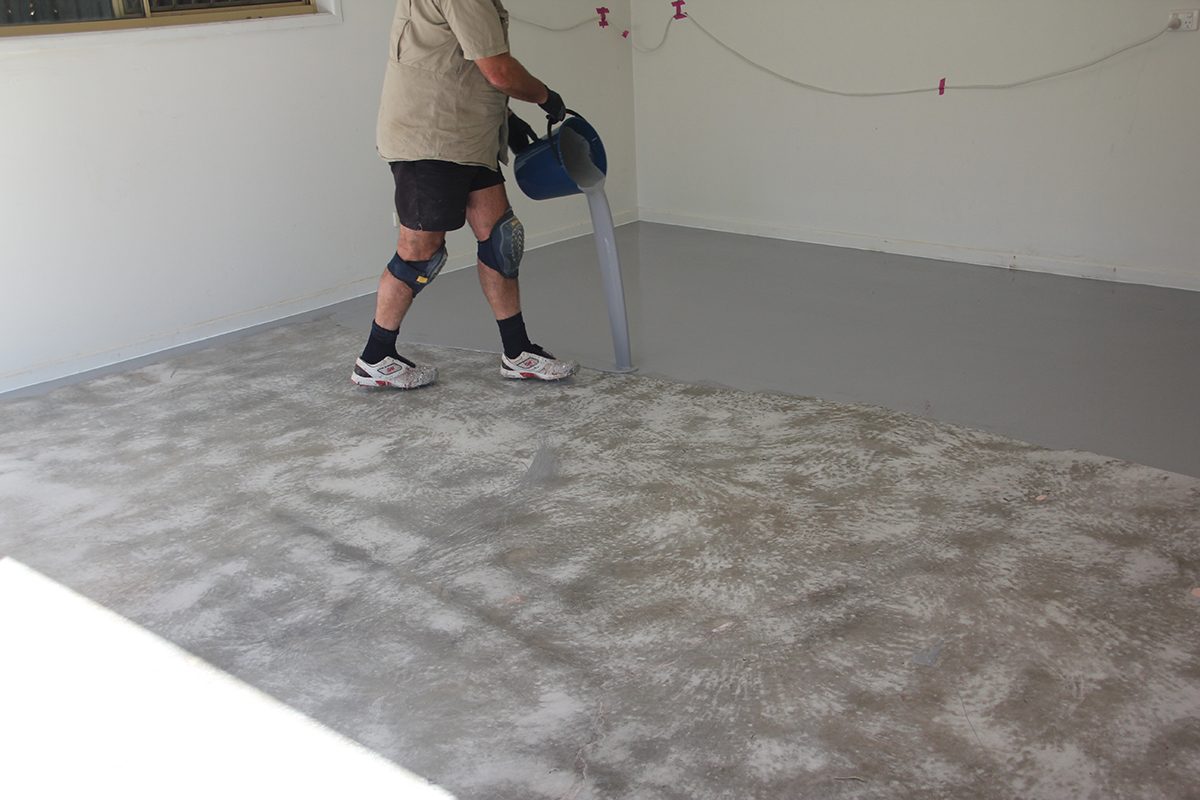 An epoxy flooring installer pouring out product from a new kit to merge with the applied film.