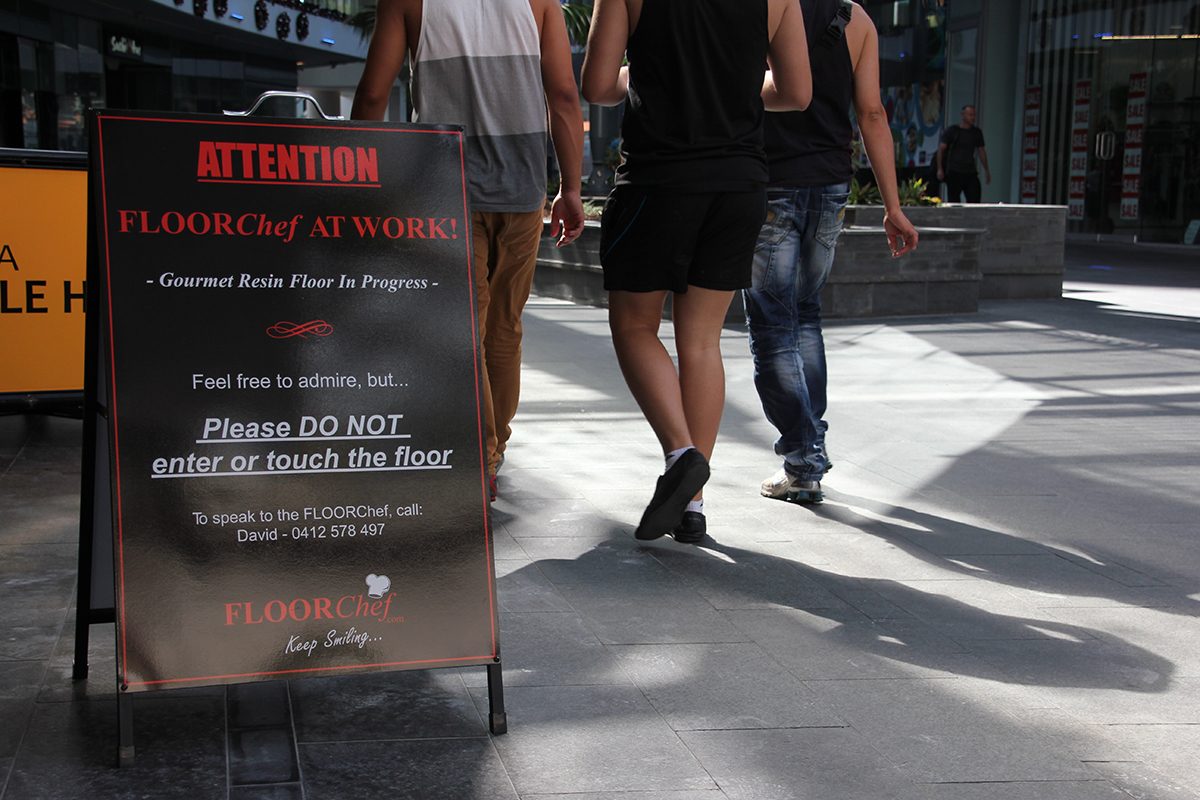 A sign outside of a restaurant warning pedestrians about the epoxy flooring installation be carried out inside.