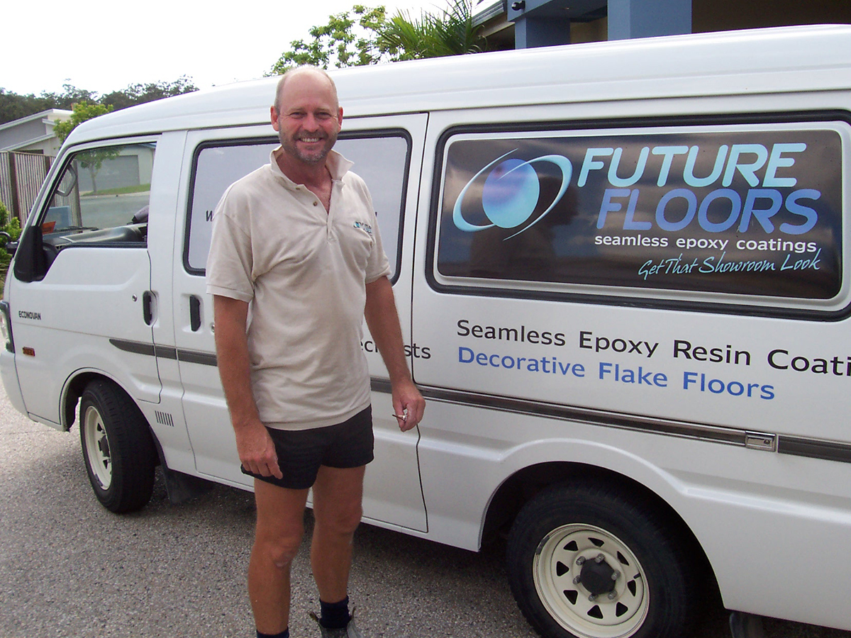 An epoxy flooring business owner smiling in front of his company vehicle.
