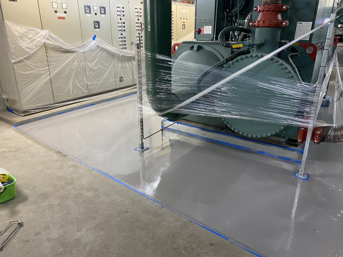 An installer applying Jaxxon coatings in a room full of pipes and fixtures on a Navy vessel.