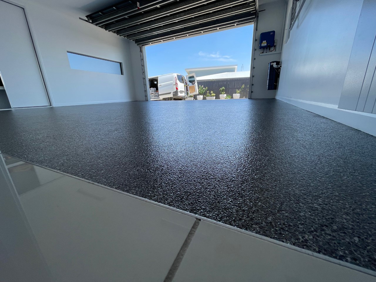 A low-angle shot of a black epoxy flake floor in a residential garage showing the gentle ripple texture of the finish.