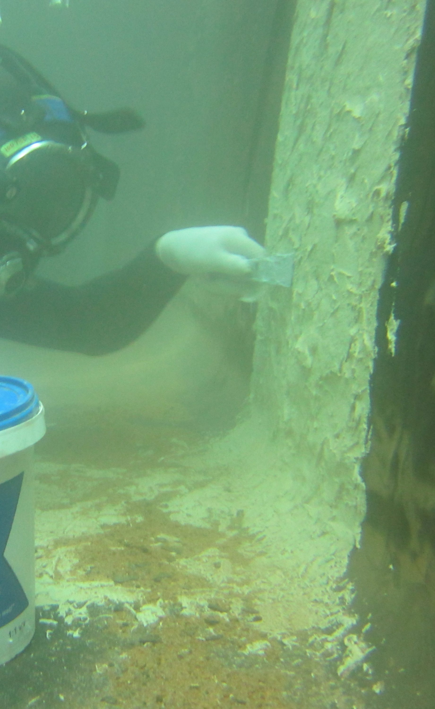 A diver using a spatula to smear Scubapoxy 1725 onto the wall of tank.