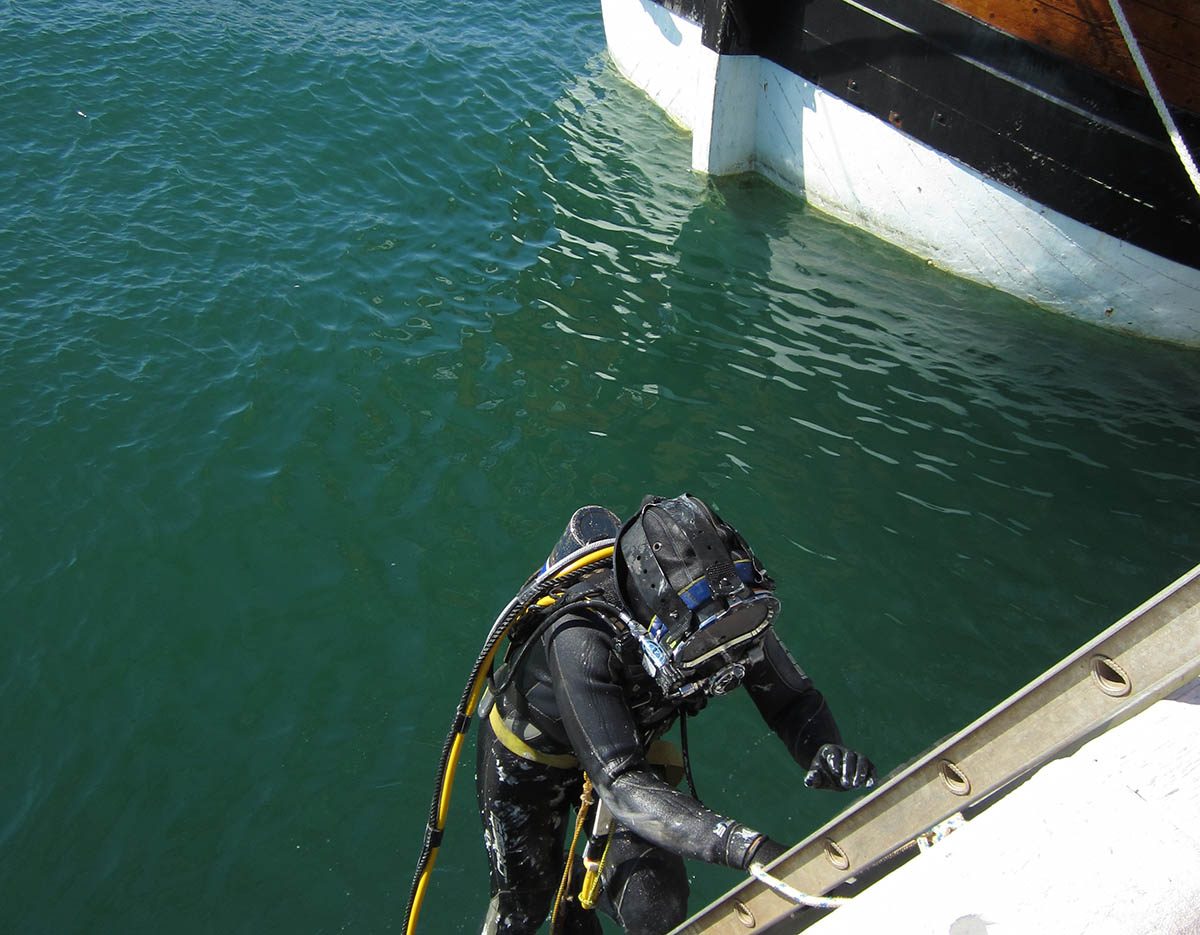 A diver entering the water before conducting repairs on the wooden hull of the ship.