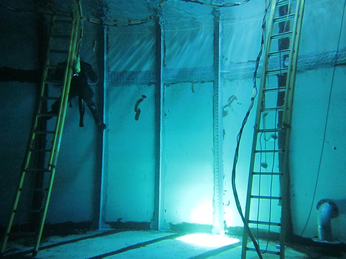 A diver floating on the side of the tank while applying Scubapoxy 1725 to seal the leaks in the seams.