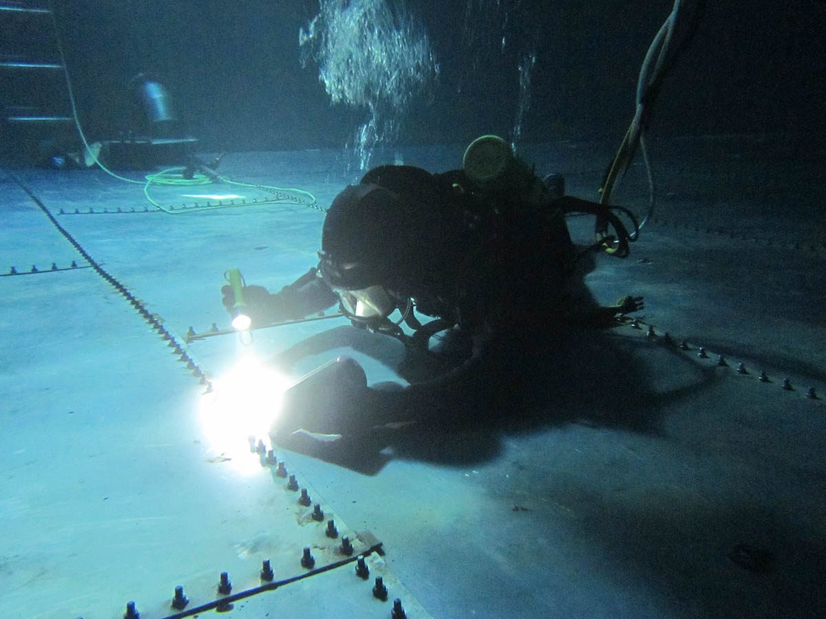 A diver conducting a leak detection exercise on the seams of the metal tank.