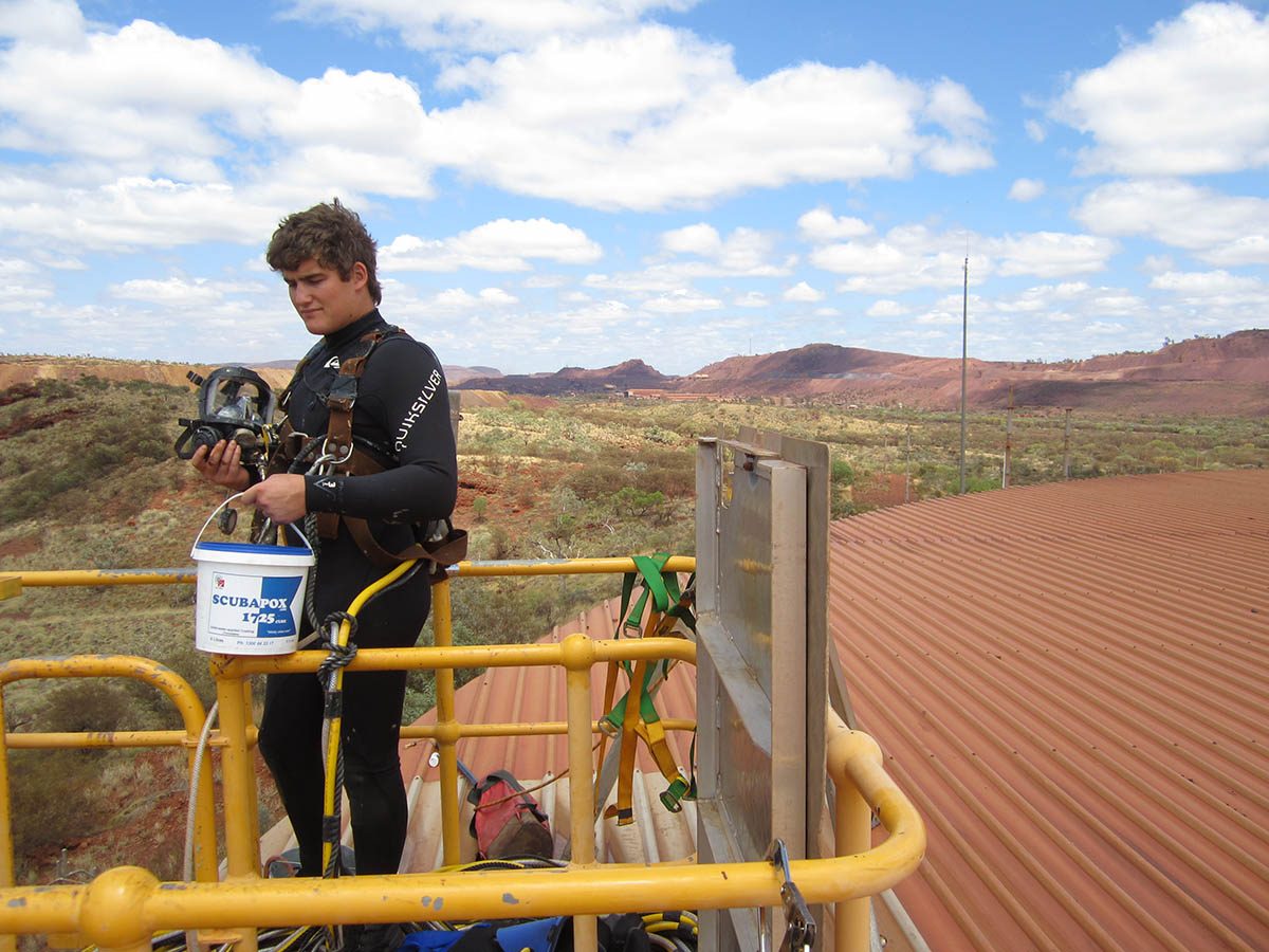 A diver standing on top of the large tank with a bucket of Scubapoxy before conducting the repairs.