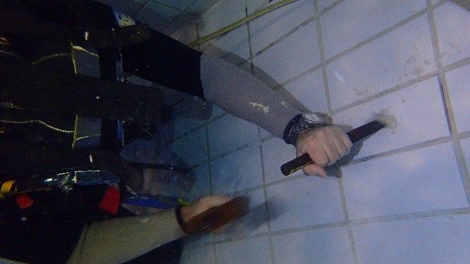A diver underwater in the swimming pool using a chisel up the loose tiles that needed to be replaced.