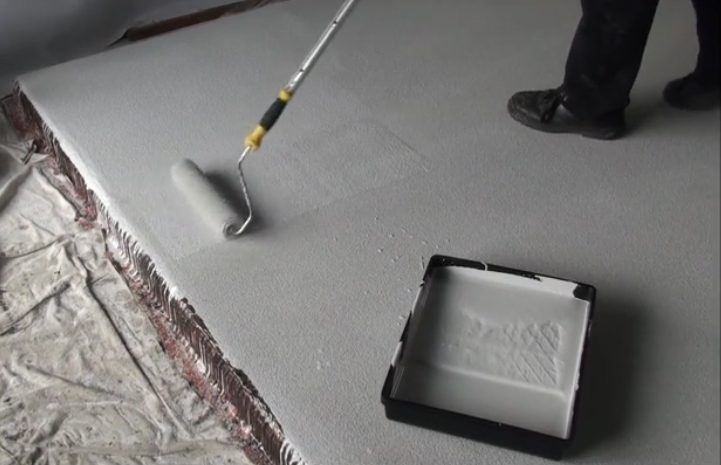 An installer works from a roller tray to apply the topcoat on a light grey, non-slip epoxy floor.