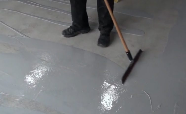 An installer using a squeegee to spread the basecoat on a light grey, protective epoxy flooring system.