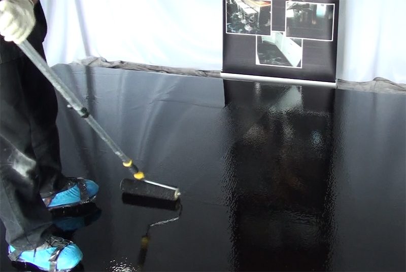 An installer rolling out a black basecoat for the metallic epoxy floor.