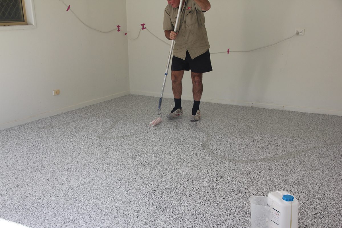 An installer rolling out the clear polyurethane topcoat for the garage epoxy flake floor.