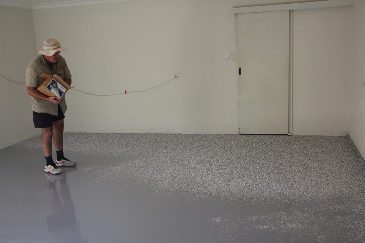An installer standing on the epoxy basecoat, tossing the flake from a box onto the wet film.