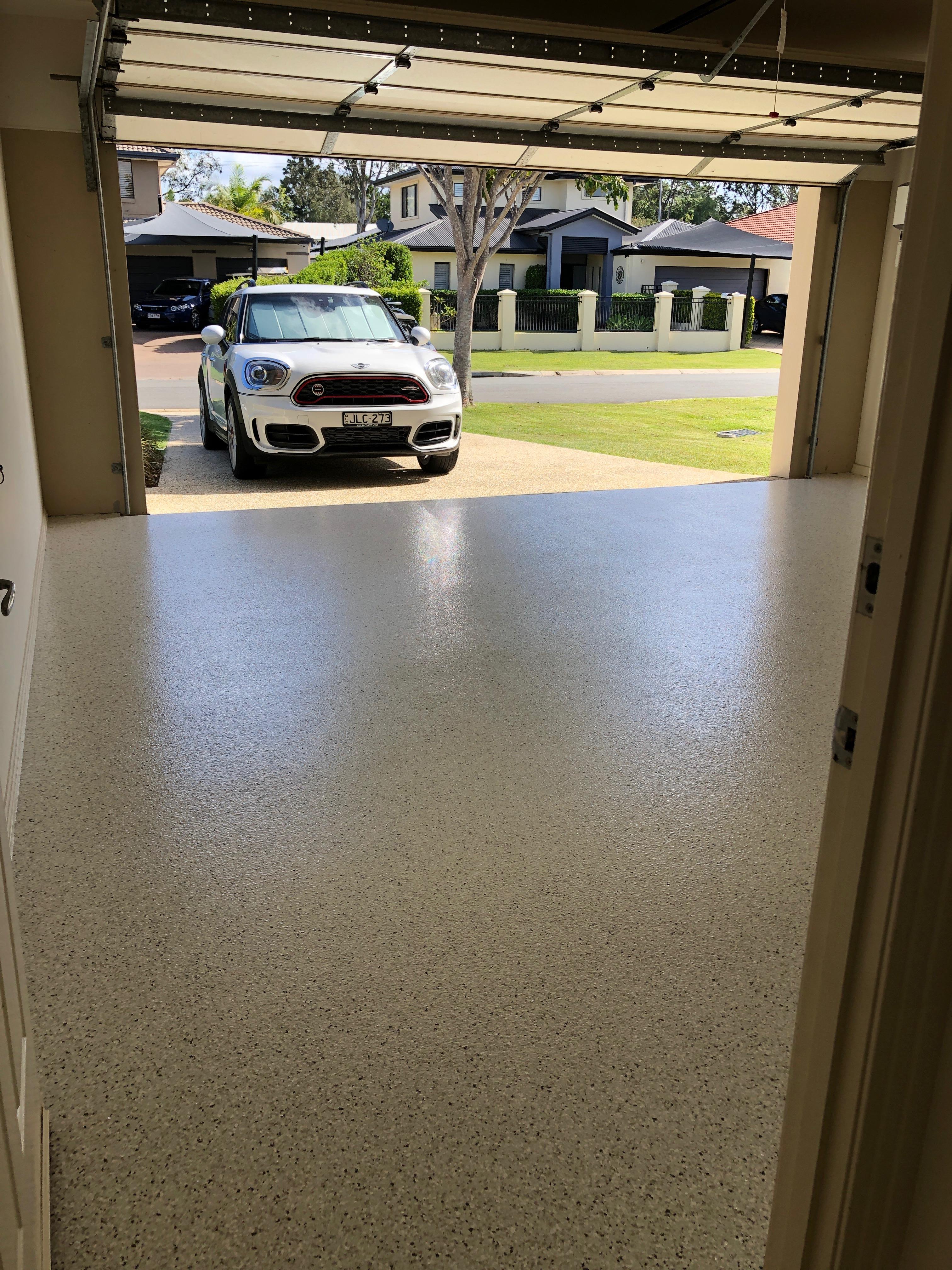 A photo taken from the back of the residential garage with the new flake floor in the foreground and car on the driveway in the background.