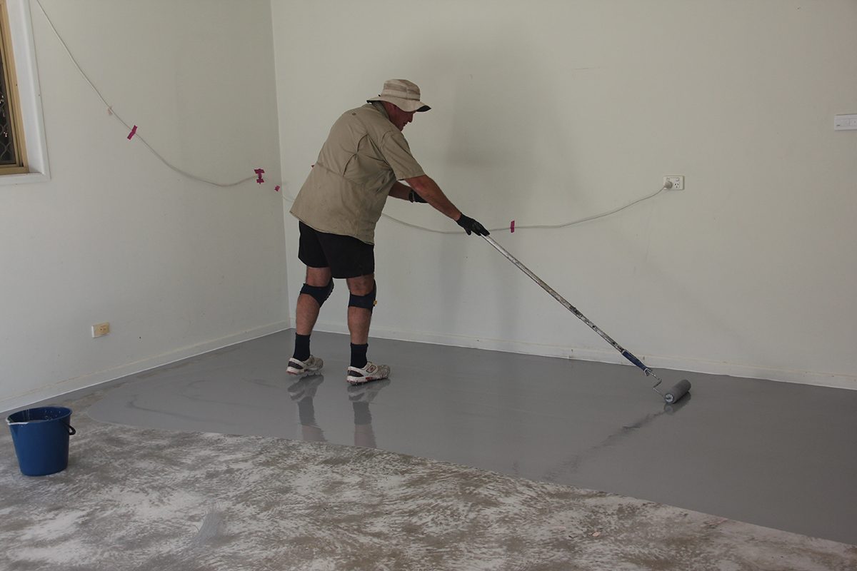 An installer uses a roller to apply epoxy flooring in a domestic garage.