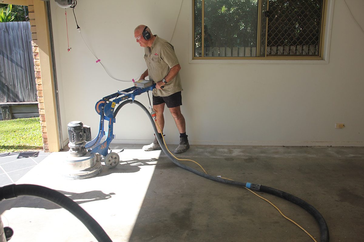 An epoxy flooring installer prepares a concrete surface with a mechanical grinder.
